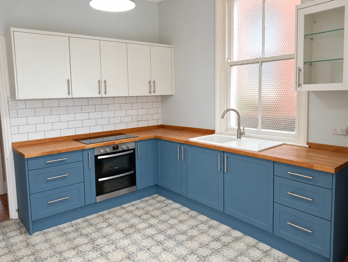 Finished kitchen with Supermatt Misty Blue base units, Supermatt White wall units, stainless steel handles, a glass display unit and the original patterned floor tiles