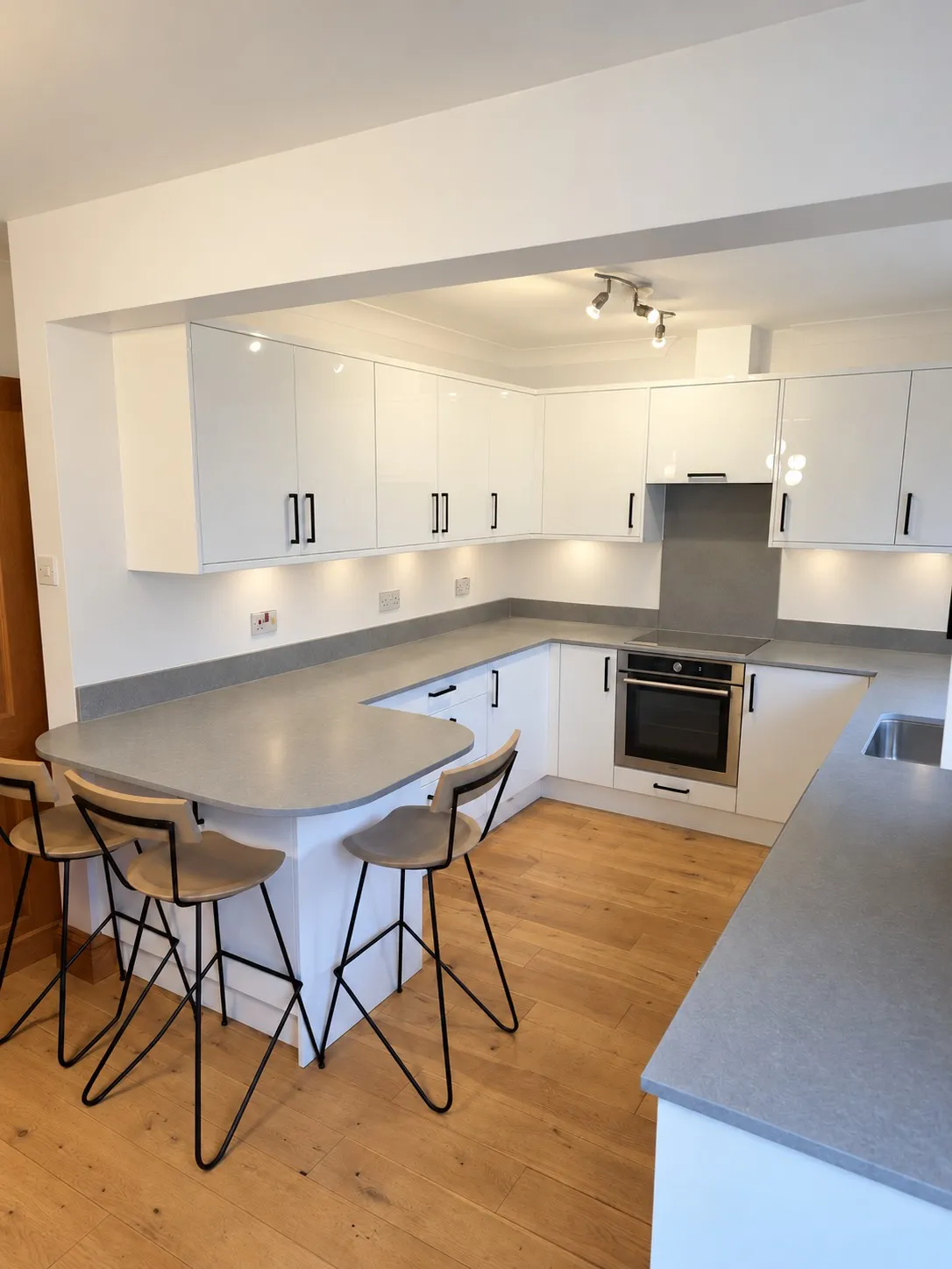 Finished kitchen with Zola gloss white doors, matt black handles, London Grey quartz worktops and a curved breakfast bar